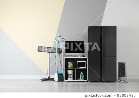 Modern refrigerator and other household appliances near color wall indoors 95802453