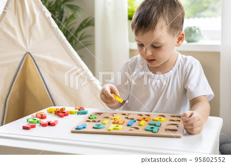 Male kid playing with wooden eco friendly alphabet letters board on table top view intellectual game Male kid playing with wooden eco friendly alphabet letters board on table top view intellectual game 95802552