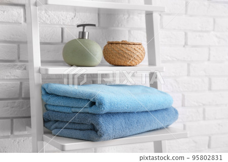 Clean soft towels and soap dispenser on shelves near white brick wall 95802831