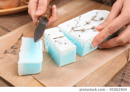 Woman cutting natural handmade soap on wooden table, closeup Woman cutting natural handmade soap on wooden table, closeup 95802904