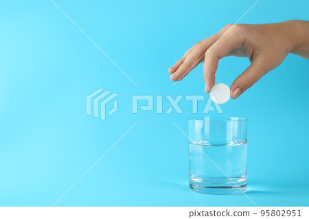 Woman putting tablet into glass of water on light blue background, space for text Woman putting tablet into glass of water on light blue background, space for text 95802951