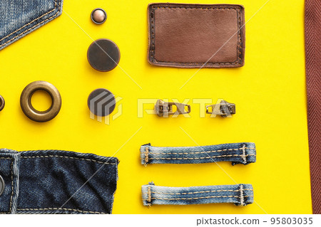 Flat lay composition with garment accessories and cutting details for jeans on yellow background Flat lay composition with garment accessories and cutting details for jeans on yellow background 95803035
