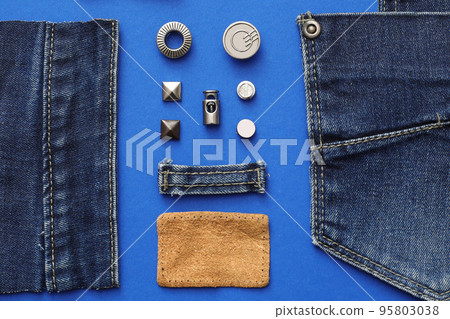 Flat lay composition with garment accessories and cutting details for jeans on blue background Flat lay composition with garment accessories and cutting details for jeans on blue background 95803038