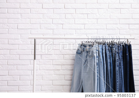 Rack with stylish jeans near brick wall Rack with stylish jeans near brick wall 95803137