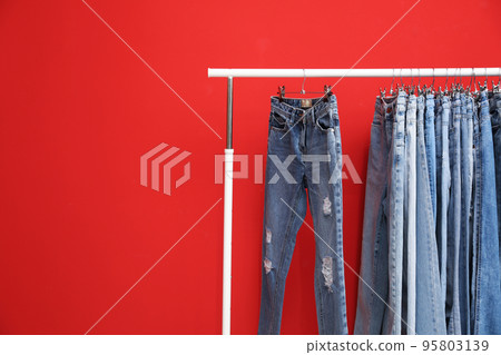 Rack with stylish jeans on red background. Space for text Rack with stylish jeans on red background. Space for text 95803139