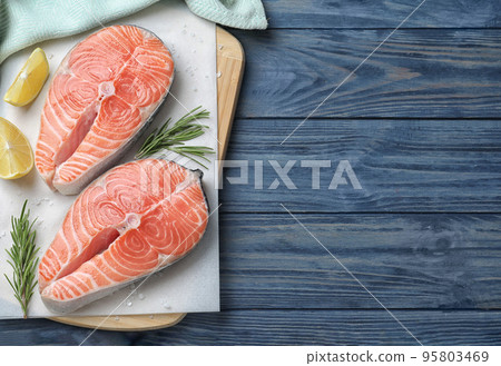 Top view of fresh raw salmon with lemon and rosemary on blue wooden table, space for text. Fish delicacy 95803469