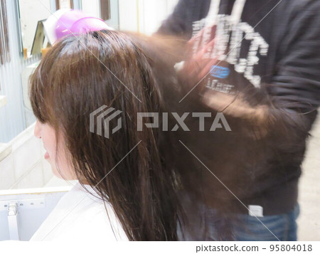 Hairdresser blowing hair of a female customer with a hair dryer Hairdresser blowing hair of a female customer with a hair dryer 95804018