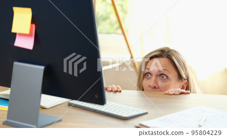 Surprised woman peeping out table and looking at pc screen Surprised woman peeping out table and looking at pc screen 95804229