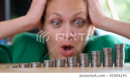 Woman looking at piles of coins and holding on head 95804245