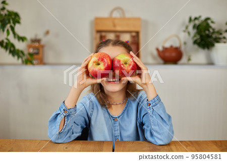 Happy emotional little girl holding red an apple in hands covering eyes at home Happy emotional little girl holding red an apple in hands covering eyes at home 95804581