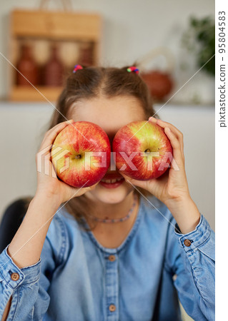 Happy emotional little girl holding red an apple in hands covering eyes at home 95804583