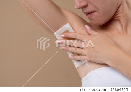Young woman doing depilation in underarms area 95804735