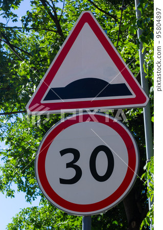 rough road sign and speed limit on a background of green trees and blue sky 95804897