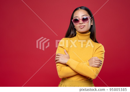 Stylish young woman in sunglasses standing against the wall Stylish young woman in sunglasses standing against the wall 95805385
