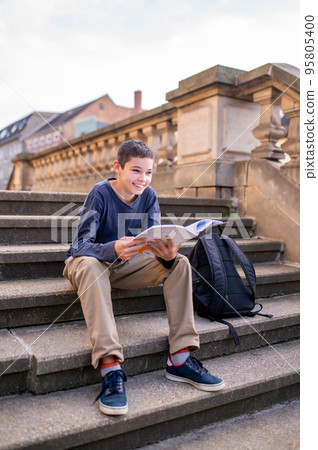 Joyous teen with a book sitting on the stairs 95805400
