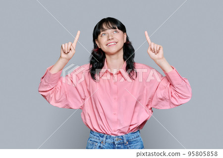 Young woman pointing fingers up, space for copyspace text, on grey background 95805858