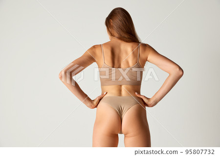 Portrait of muscular female back, waist and buttocks isolated on grey background. Model posing in underwear. Sportive body shape Portrait of muscular female back, waist and buttocks isolated on grey background. Model posing in underwear. Sportive body shape 95807732
