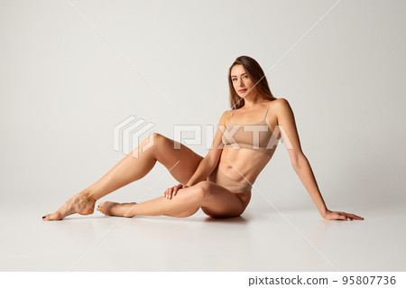 Portrait of beautiful woman with slim figure posing in underwear isolated over grey background. Muscular body shape 95807736