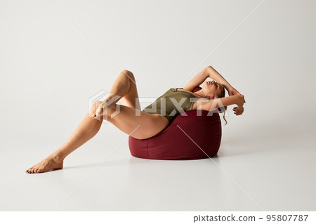 Portrait of beautiful slim woman posing in green bodysuit on floor pillow over grey studio background. Femininity and wellbeing Portrait of beautiful slim woman posing in green bodysuit on floor pillow over grey studio background. Femininity and wellbeing 95807787