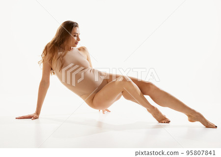 Portrait of beautiful woman posing in beige bodysuit over white studio background. Slim smooth legs Portrait of beautiful woman posing in beige bodysuit over white studio background. Slim smooth legs 95807841