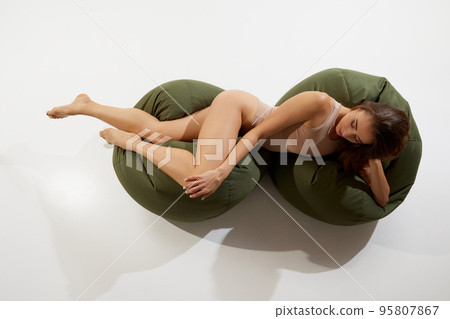 Portrait of beautiful slim woman in beige underwear posing on floor pillows isolated on white background. Top view Portrait of beautiful slim woman in beige underwear posing on floor pillows isolated on white background. Top view 95807867
