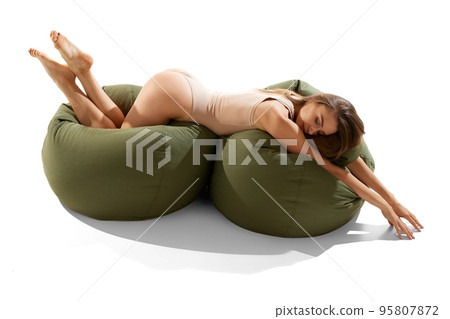 Portrait of beautiful slim woman in beige underwear posing on floor pillows isolated on white background. Sensuality 95807872