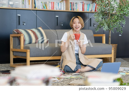 Young woman spreading papers on the floor and drinking a drink while working 95809029
