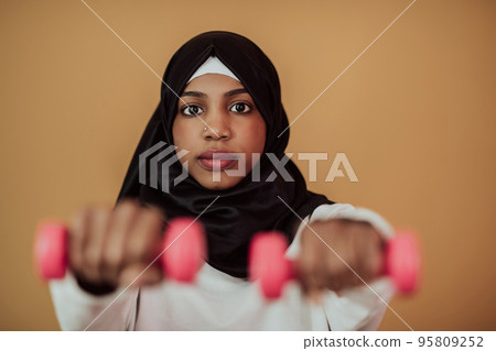 Afro muslim woman promotes a healthy life, holding dumbbells in her hands 95809252