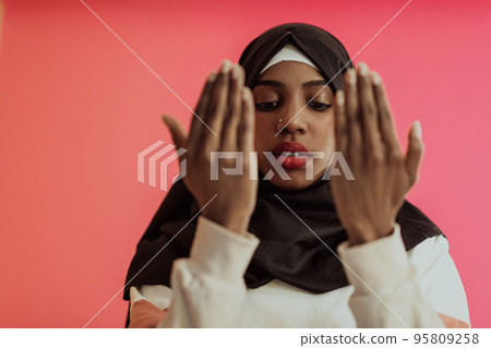 African muslim woman wearing hijab and traditional muslim clothes posing in front of red background African muslim woman wearing hijab and traditional muslim clothes posing in front of red background 95809258