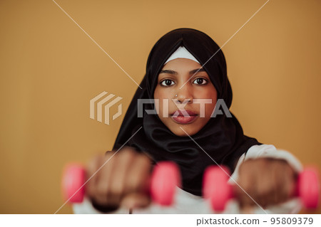 Afro muslim woman promotes a healthy life, holding dumbbells in her hands Afro muslim woman promotes a healthy life, holding dumbbells in her hands 95809379