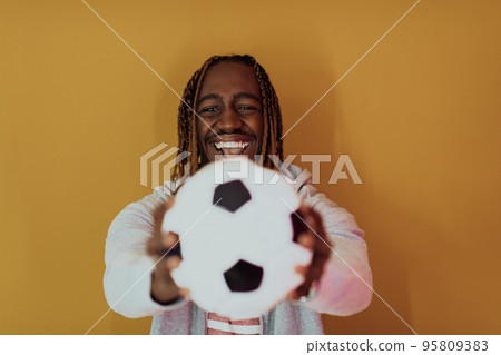 Afro man posing on a yellow background while holding a soccer ball 95809383