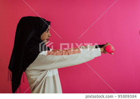 Afro muslim woman promotes a healthy life, holding dumbbells in her hands Afro muslim woman promotes a healthy life, holding dumbbells in her hands 95809384