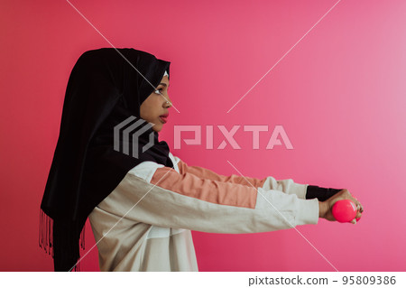 Afro muslim woman promotes a healthy life, holding dumbbells in her hands 95809386