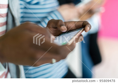 Diverse teenagers using mobile devices while posing for a studio photo in front of a colorful background 95809478
