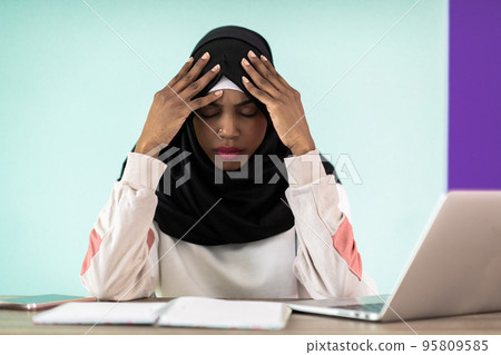 afro girl wearing a hijab is disappointed and sad sitting in her home office and using a laptop 95809585