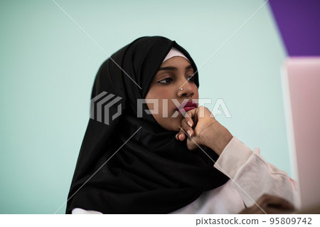 afro girl wearing a hijab is disappointed and sad sitting in her home office and using a laptop afro girl wearing a hijab is disappointed and sad sitting in her home office and using a laptop 95809742