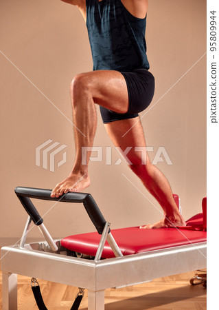 Handsome pilates male instructor performing stretching balance fitness exercise on small barrel equipment, at the pilates studio modern onterior indoor. 95809944