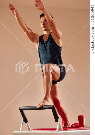 Fit man doing a lunge stretch yoga pilates exercise to strengthen and tone his muscles using a reformer in a gym 95809945