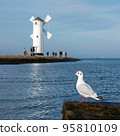 Gull bird resting on breakwater with blured old windmill lighthouse a port in Poland on the Baltic Sea 95810109
