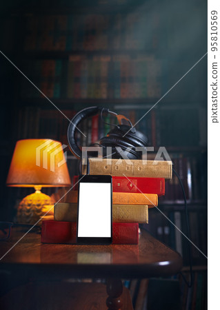 Mobile phone, headphones and a stack of books near the lamp. Concept of training and audiobooks. Library bookcase in the background. Copy space and Mock up Mobile phone, headphones and a stack of books near the lamp. Concept of training and audiobooks. Library bookcase in the background. Copy space and Mock up 95810569
