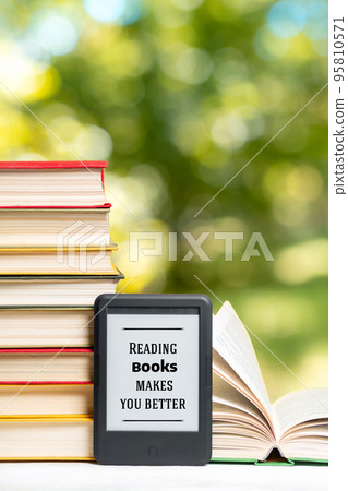 Reading. E-book reader and a stack of books. The park is blurred in the background. Copy space. Vertical. Concept of education and electronic gadgets 95810571