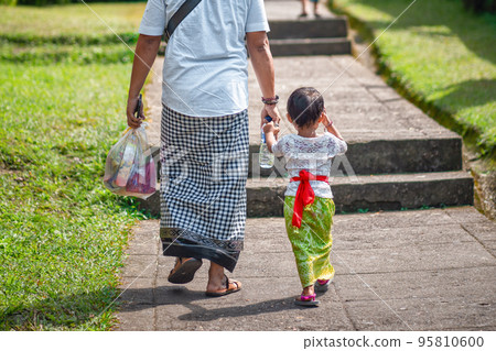 Father and son hold hands and walk together along the path. Indonesian culture. island of Bali. Close up Father and son hold hands and walk together along the path. Indonesian culture. island of Bali. Close up 95810600