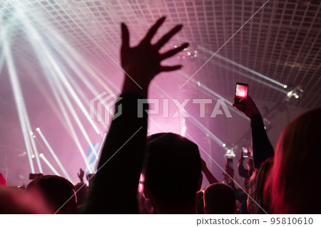 A crowd of people at the concert have fun and dance to the music at the concert. Rear view. Hand close up. The concept of entertainment and relaxation 95810610