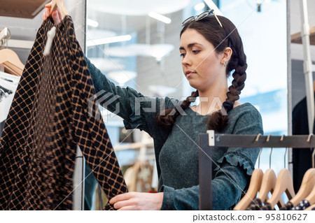 Portrait of a young Caucasian woman looking for clothes in a store. The concept of consumerism Portrait of a young Caucasian woman looking for clothes in a store. The concept of consumerism 95810627