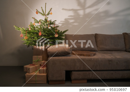 Small christmas tree with natural decorations and presents indoor near couch with warm light Small christmas tree with natural decorations and presents indoor near couch with warm light 95810697