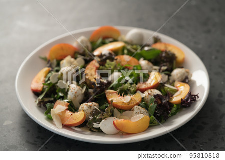 Closeup salad with nectarines, mozzarella and mixed greens in white plate on concrete background 95810818