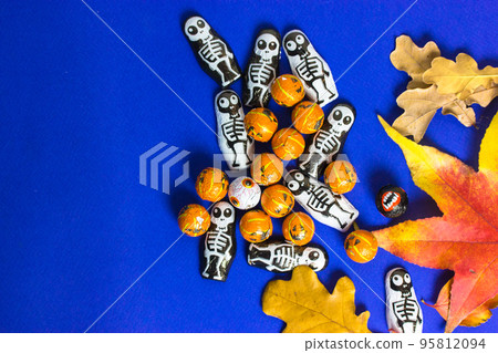 Trick o treat skeletons, pumpkins, fallen autumn maple, oak leaves on blue background with copy space. Halloween party celebration fun concept. Invitation to a party October 31st. Sweets for kids Trick o treat skeletons, pumpkins, fallen autumn maple, oak leaves on blue background with copy space. Halloween party celebration fun concept. Invitation to a party October 31st. Sweets for kids 95812094