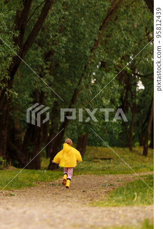 Happy funny baby under autumn shower. Girl running merrily laughing in the rain 95812439