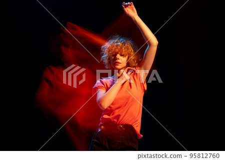 Contemp dance. Young attractive girl with short curly red hair dancing isolated over black background in mixed orange light. Art, beauty, fashion, trendy style Contemp dance. Young attractive girl with short curly red hair dancing isolated over black background in mixed orange light. Art, beauty, fashion, trendy style 95812760