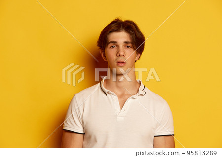 Portrait of young man in casual white T-shirt posing with shocked expression over yellow background Portrait of young man in casual white T-shirt posing with shocked expression over yellow background 95813289
